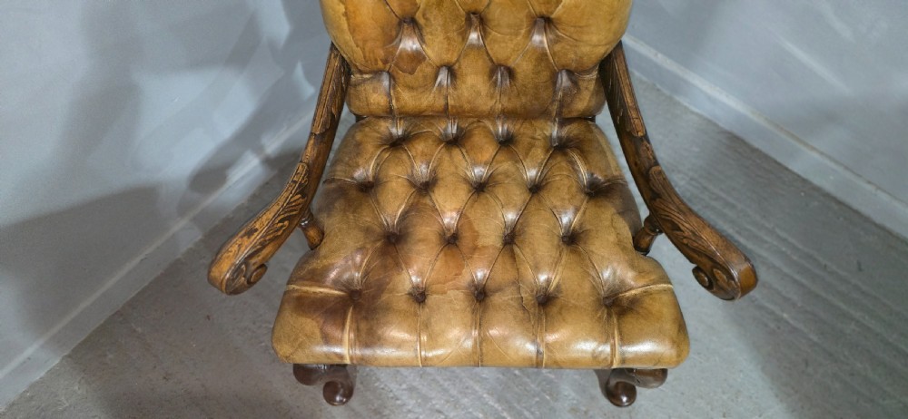 An antique William and Mary style high-back armchair upholstered in deep-buttoned tan leather with carved walnut arms and legs. View VIII