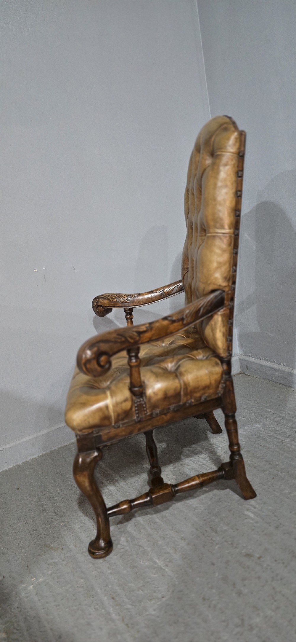 An antique William and Mary style high-back armchair upholstered in deep-buttoned tan leather with carved walnut arms and legs. View IX