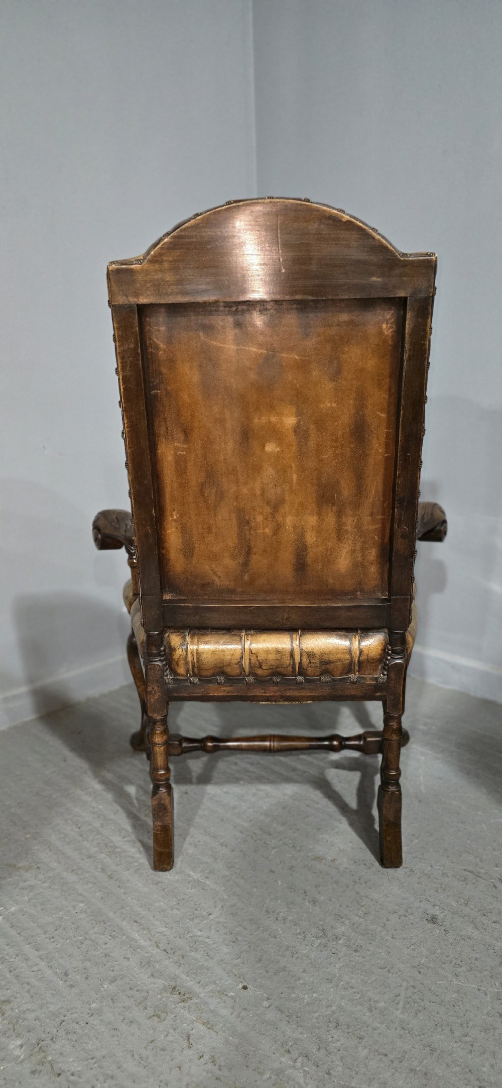 An antique William and Mary style high-back armchair upholstered in deep-buttoned tan leather with carved walnut arms and legs. View XI
