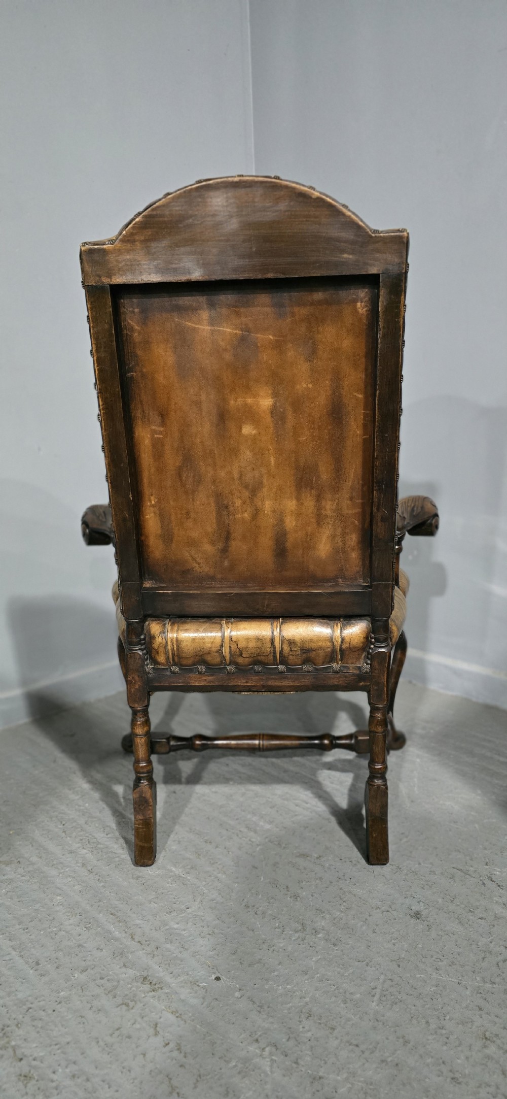 An antique William and Mary style high-back armchair upholstered in deep-buttoned tan leather with carved walnut arms and legs. View XII