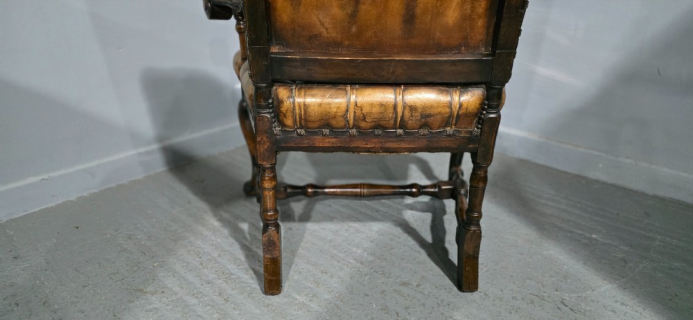 An antique William and Mary style high-back armchair upholstered in deep-buttoned tan leather with carved walnut arms and legs. View XIII
