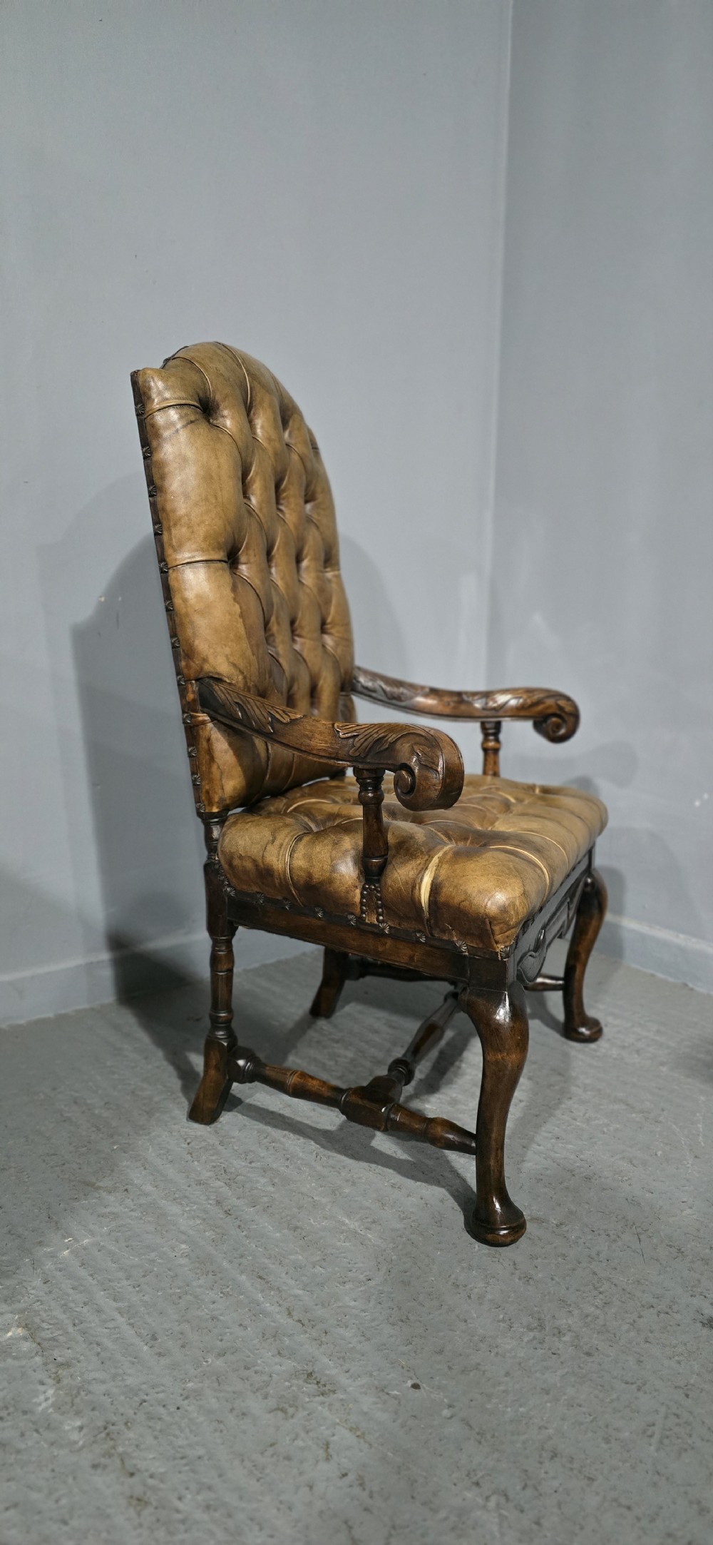 An antique William and Mary style high-back armchair upholstered in deep-buttoned tan leather with carved walnut arms and legs. View XV