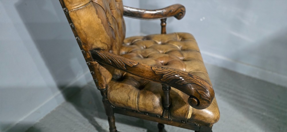 An antique William and Mary style high-back armchair upholstered in deep-buttoned tan leather with carved walnut arms and legs. View XVI