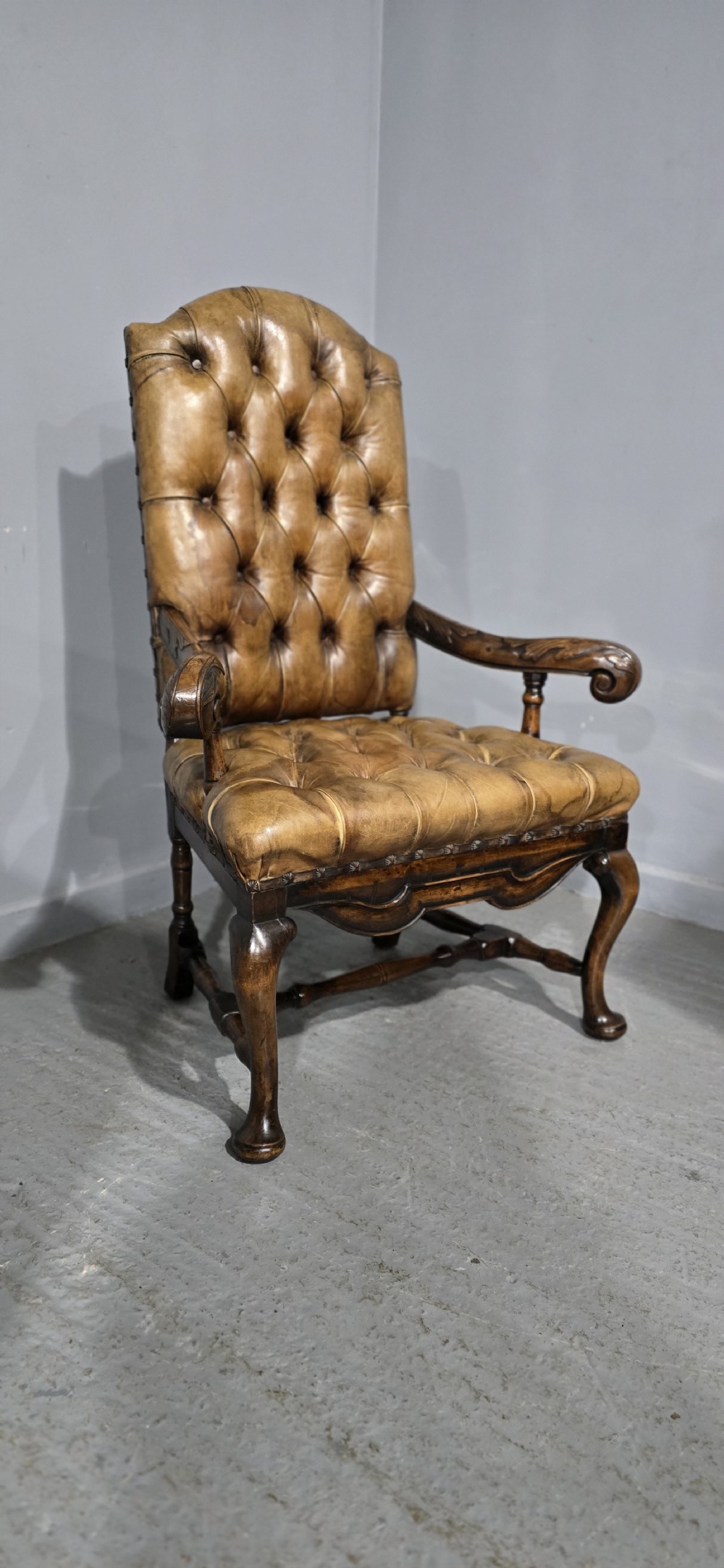 An antique William and Mary style high-back armchair upholstered in deep-buttoned tan leather with carved walnut arms and legs. View XVII