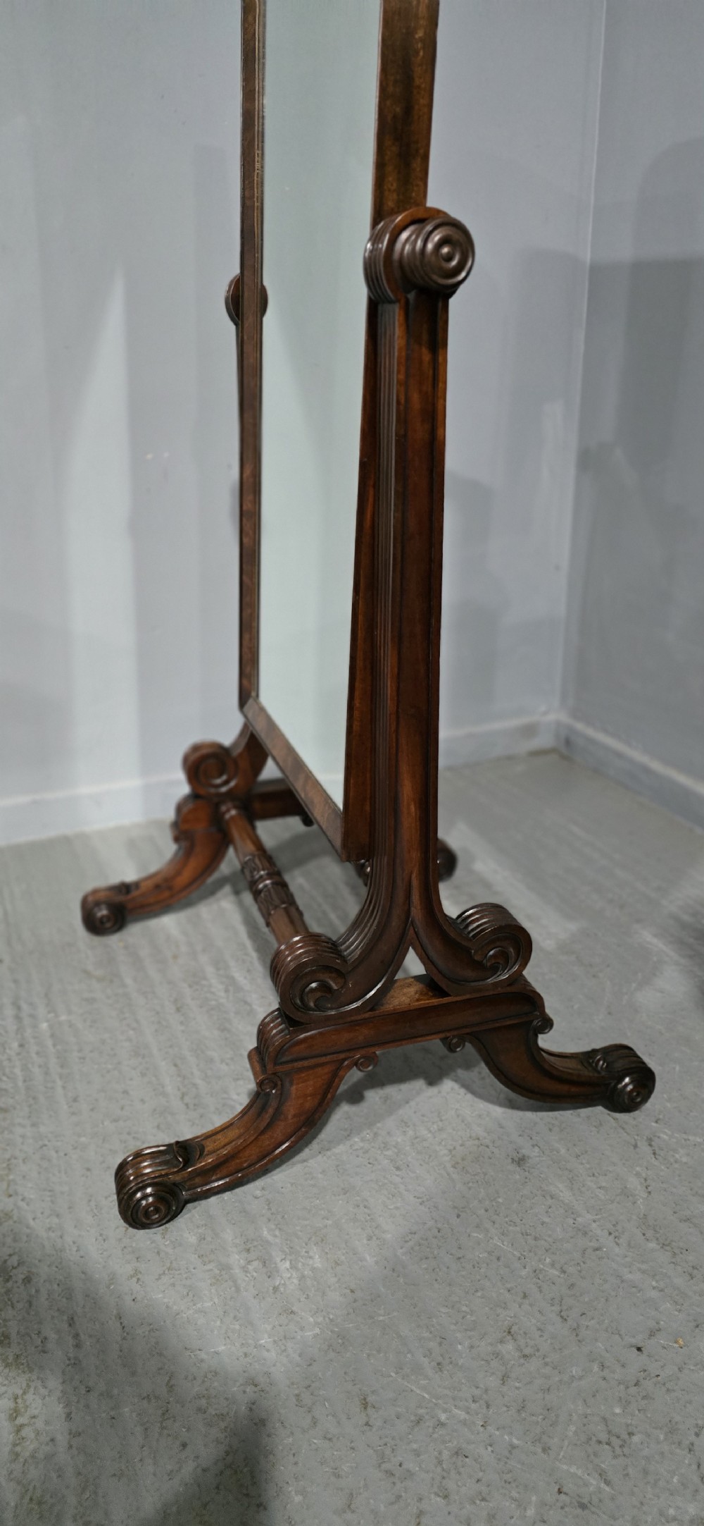 An antique Regency mahogany cheval mirror featuring a rectangular frame set between reeded upright posts on splayed legs. View VII
