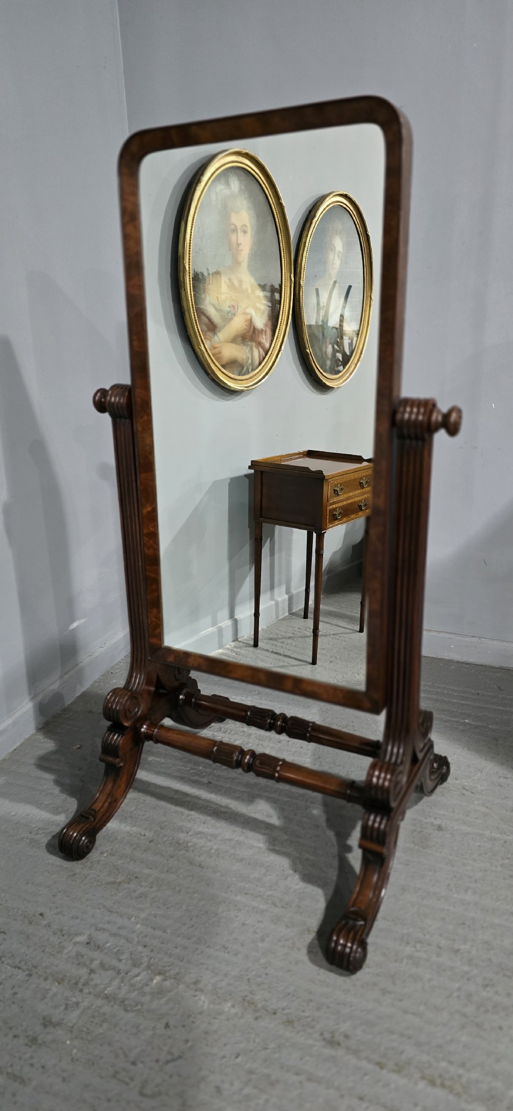 An antique Regency mahogany cheval mirror featuring a rectangular frame set between reeded upright posts on splayed legs. View XI
