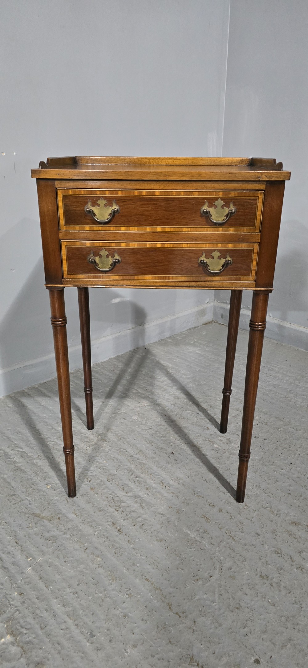 A dark mahogany side table featuring two drawers with brass batwing drop handles, crossbanded inlay borders, and slender turned legs. View II