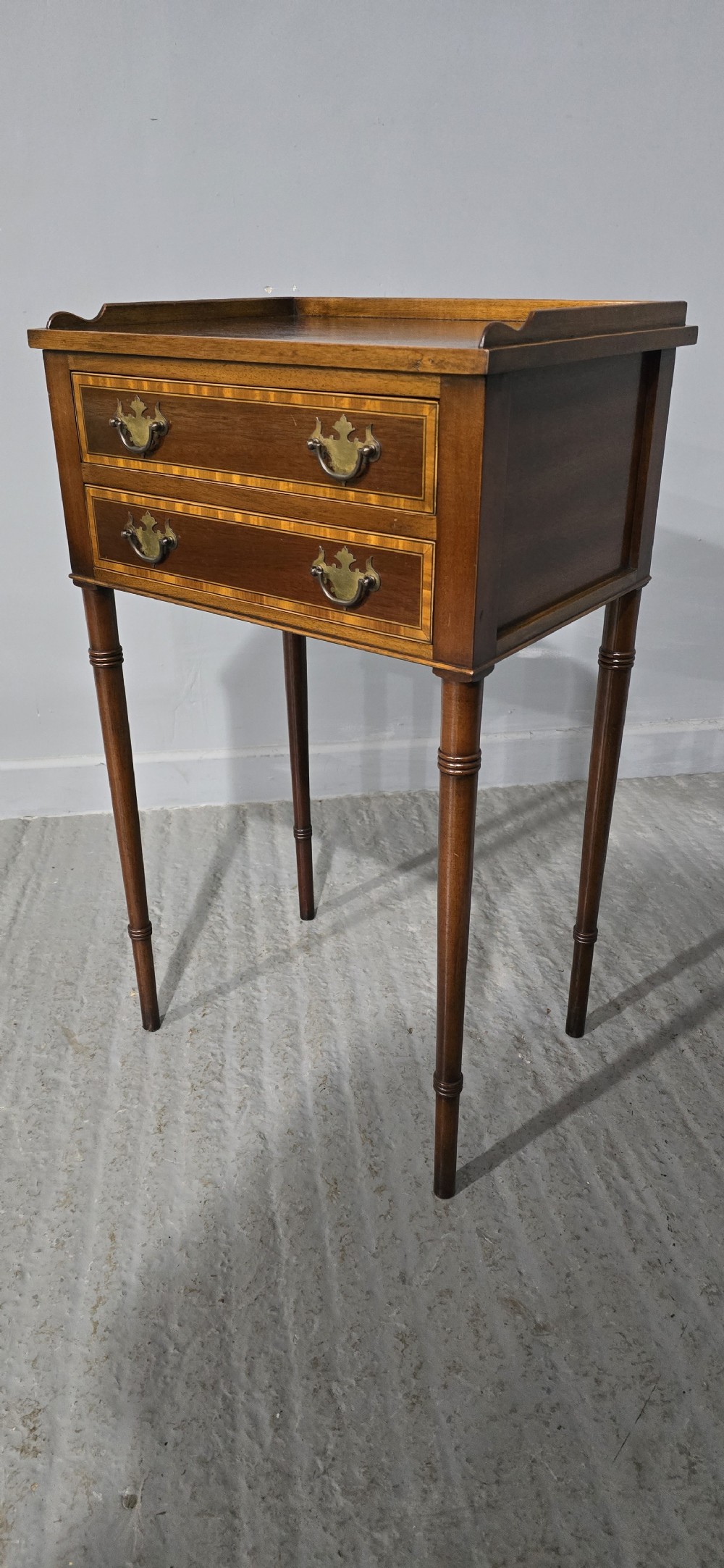 A dark mahogany side table featuring two drawers with brass batwing drop handles, crossbanded inlay borders, and slender turned legs. View III