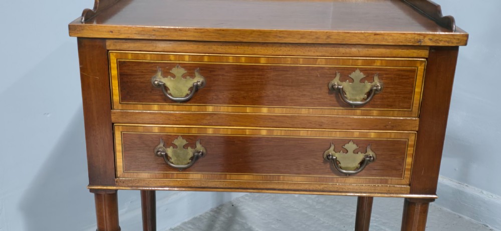 A dark mahogany side table featuring two drawers with brass batwing drop handles, crossbanded inlay borders, and slender turned legs. View VI