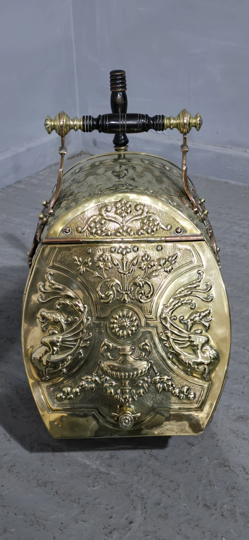 An embossed Victorian brass and copper coal scuttle with a turned wooden handle and detailed feet. View II