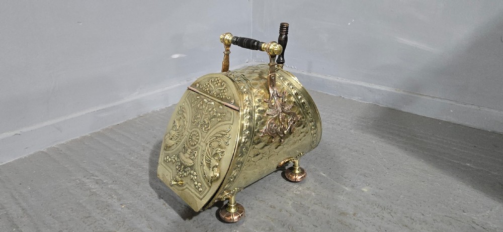 An embossed Victorian brass and copper coal scuttle with a turned wooden handle and detailed feet. View IV
