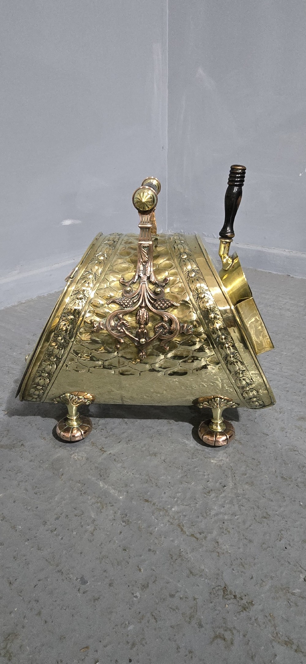 An embossed Victorian brass and copper coal scuttle with a turned wooden handle and detailed feet. View V