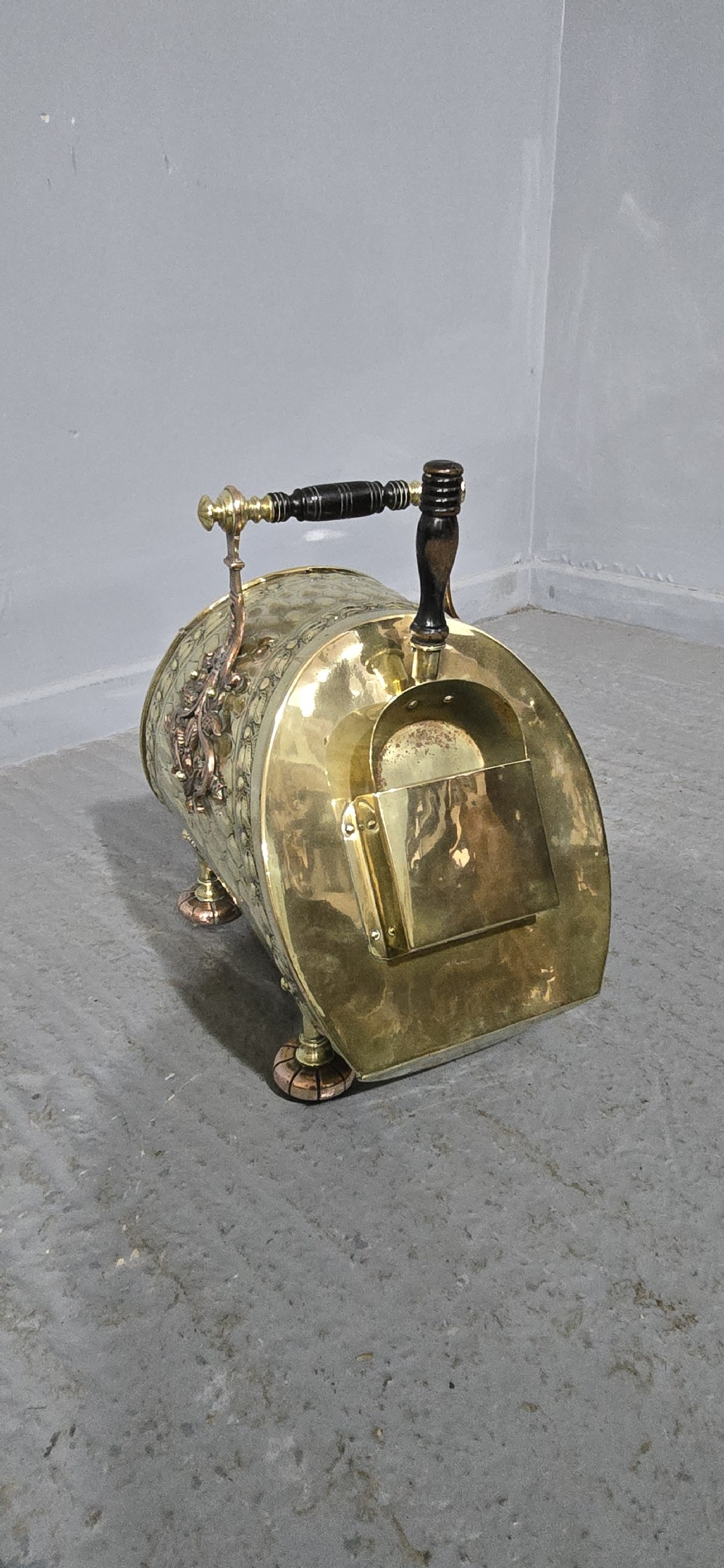 An embossed Victorian brass and copper coal scuttle with a turned wooden handle and detailed feet. View VI