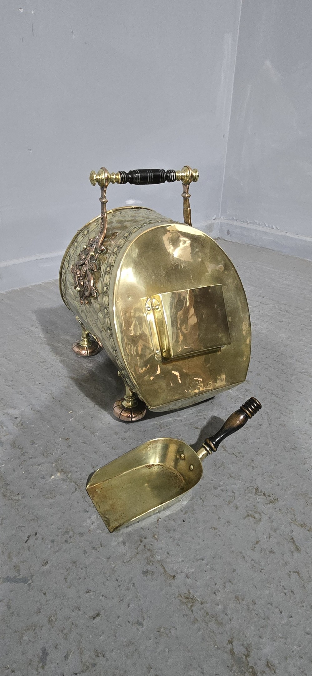 An embossed Victorian brass and copper coal scuttle with a turned wooden handle and detailed feet. View VII