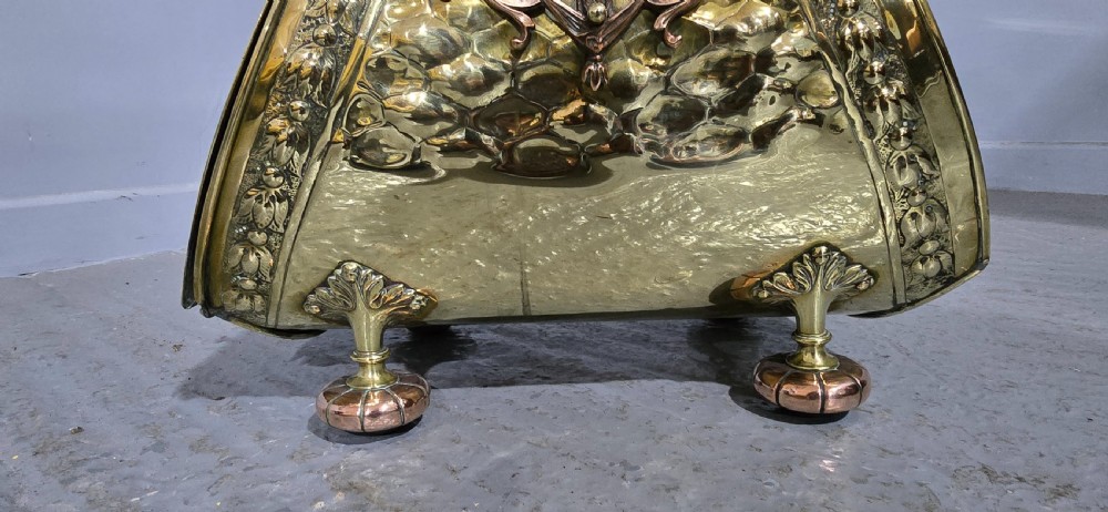 An embossed Victorian brass and copper coal scuttle with a turned wooden handle and detailed feet. View VIII
