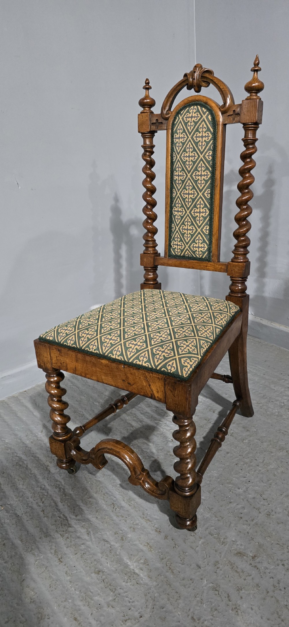 An antique walnut hall chair featuring spiral barley twist legs and supports, a carved crest with finials, and green patterned textile upholstery on the seat and backrest. View II