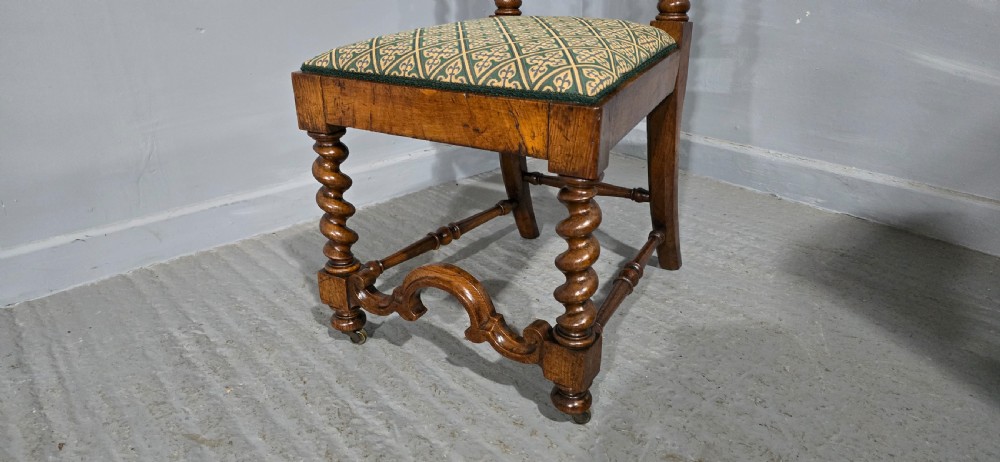 An antique walnut hall chair featuring spiral barley twist legs and supports, a carved crest with finials, and green patterned textile upholstery on the seat and backrest. View V