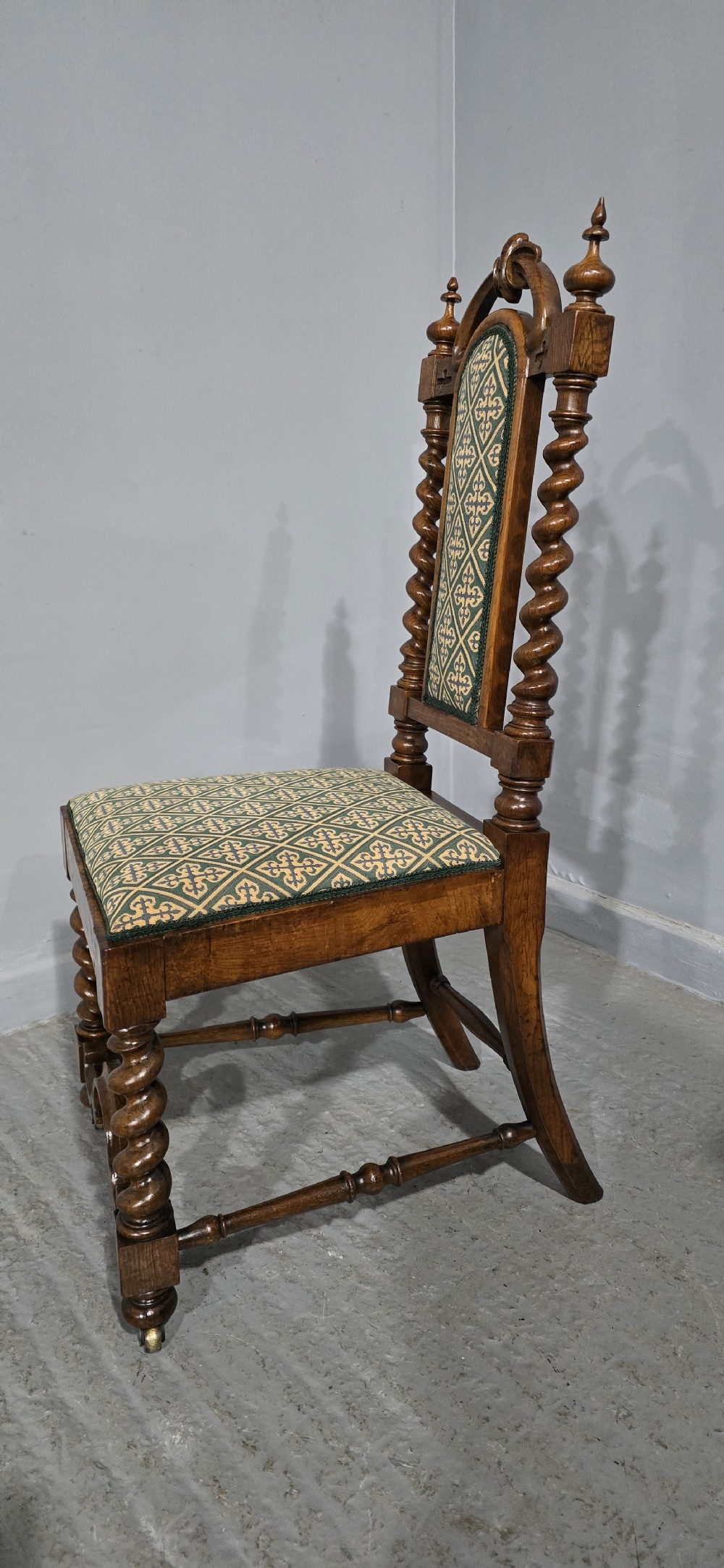 An antique walnut hall chair featuring spiral barley twist legs and supports, a carved crest with finials, and green patterned textile upholstery on the seat and backrest. View VIII