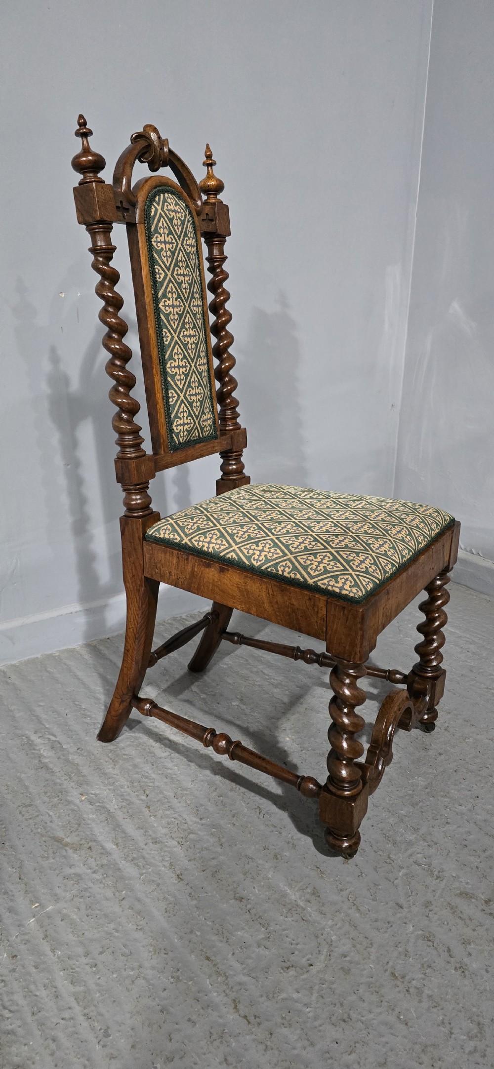 An antique walnut hall chair featuring spiral barley twist legs and supports, a carved crest with finials, and green patterned textile upholstery on the seat and backrest. View X