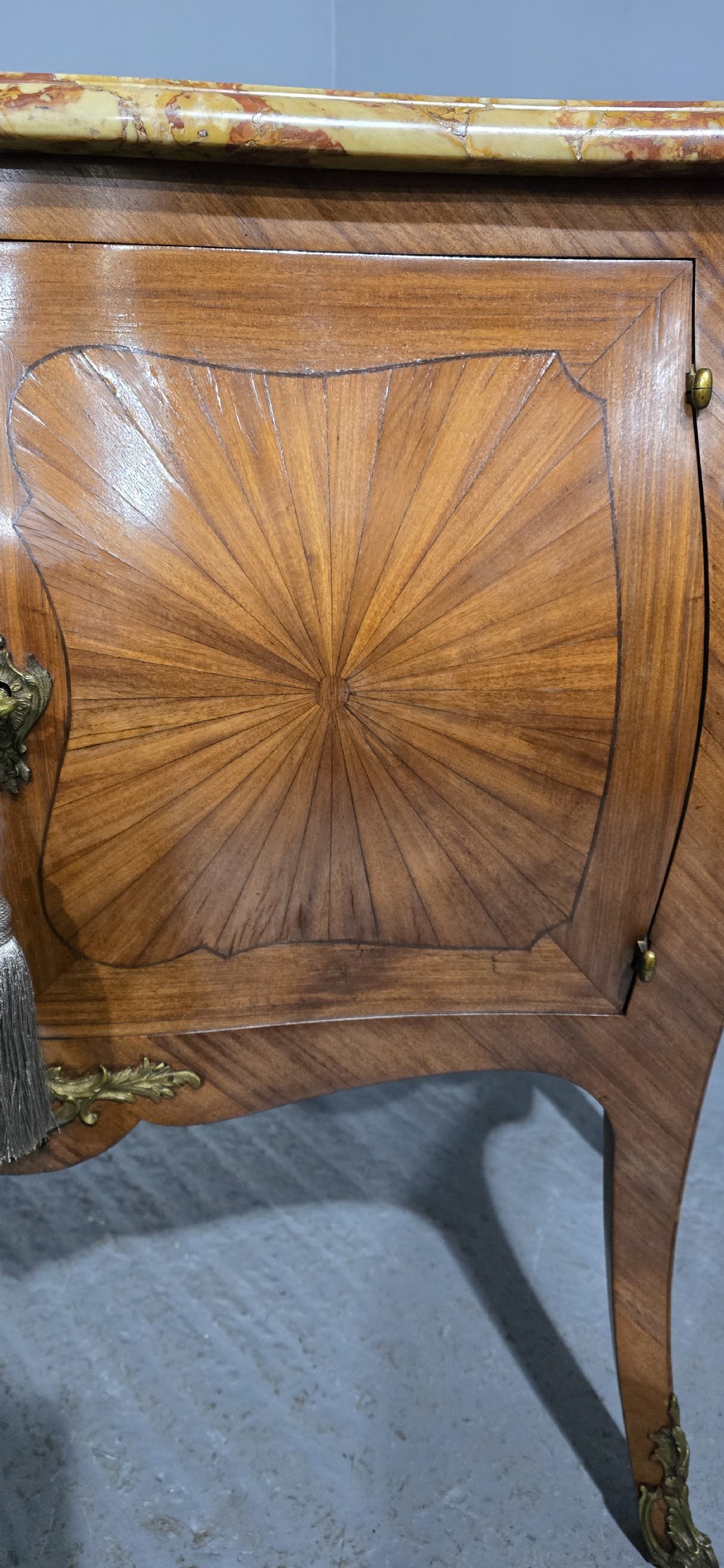 A French Louis XV style two-door cabinet featuring sunburst parquetry woodwork, a variegated marble top, cabriole legs, and ornate gilt bronze mounts. View V