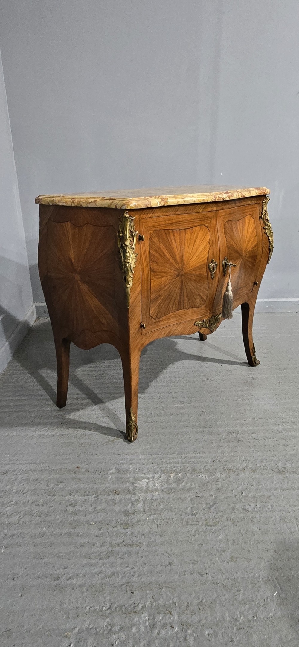 A French Louis XV style two-door cabinet featuring sunburst parquetry woodwork, a variegated marble top, cabriole legs, and ornate gilt bronze mounts. View XVI