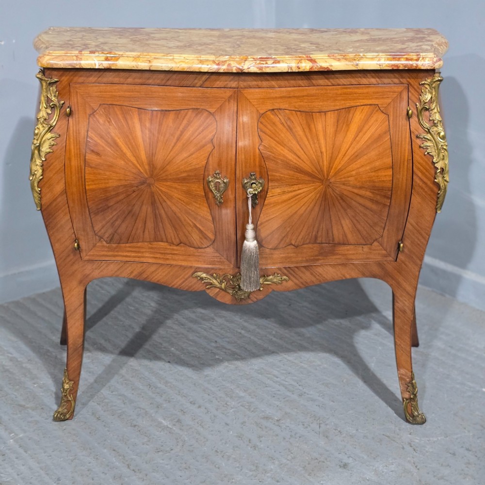 A French Louis XV style two-door cabinet featuring sunburst parquetry woodwork, a variegated marble top, cabriole legs, and ornate gilt bronze mounts.