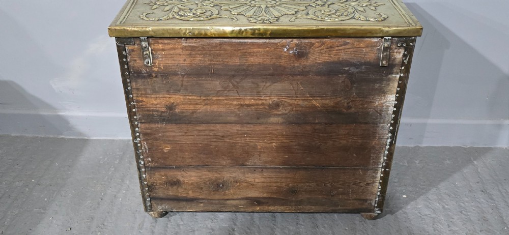 A rectangular Victorian brass log bin featuring detailed repousse relief panels of figures inside a domestic hearth interior. View IX