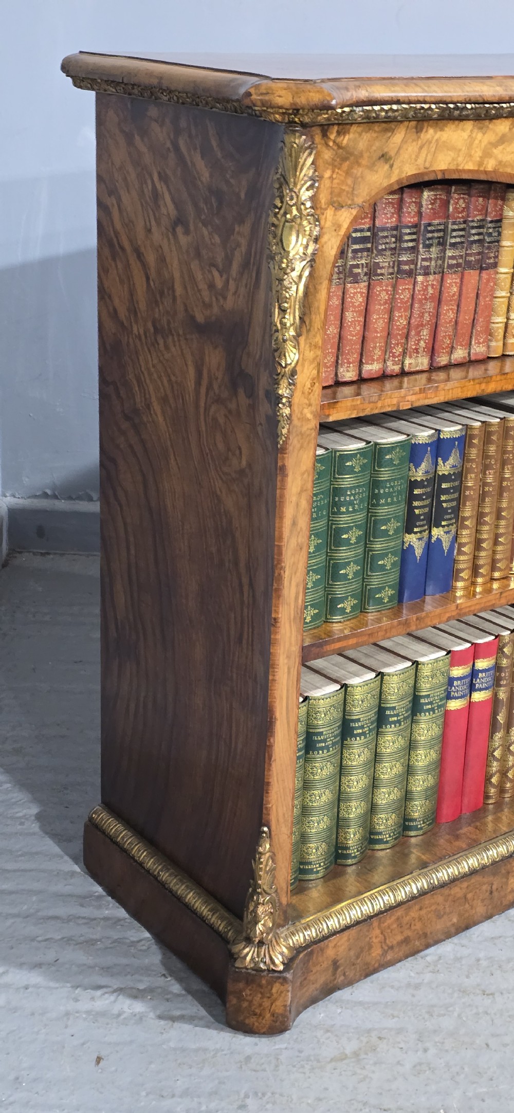 An antique open walnut library bookcase featuring three exposed shelves and decorative gilt bronze mounts along the upper apron and corner supports. View VII