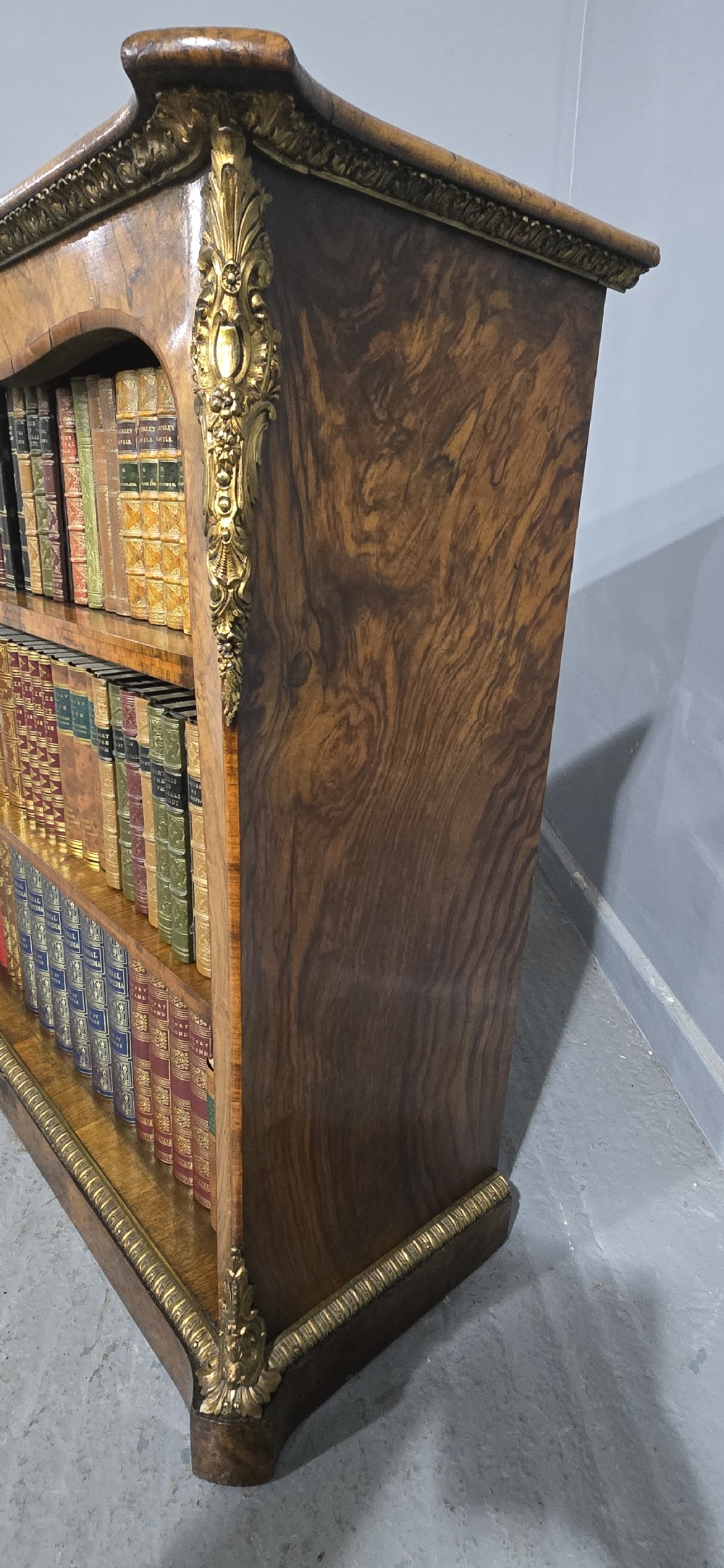 An antique open walnut library bookcase featuring three exposed shelves and decorative gilt bronze mounts along the upper apron and corner supports. View XVI