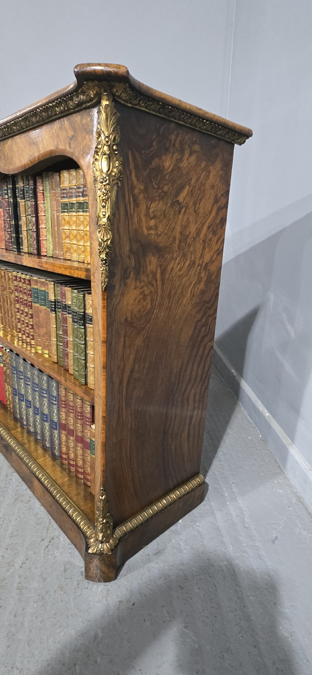 An antique open walnut library bookcase featuring three exposed shelves and decorative gilt bronze mounts along the upper apron and corner supports. View XVII