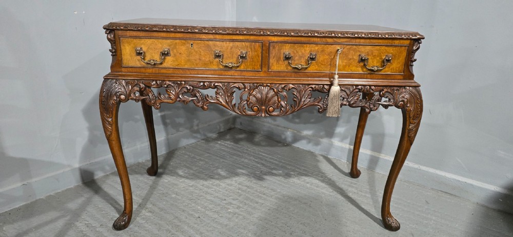 A burr walnut console table featuring two drawers with brass handles, a deeply carved apron with a central shell motif, and cabriole legs. View III