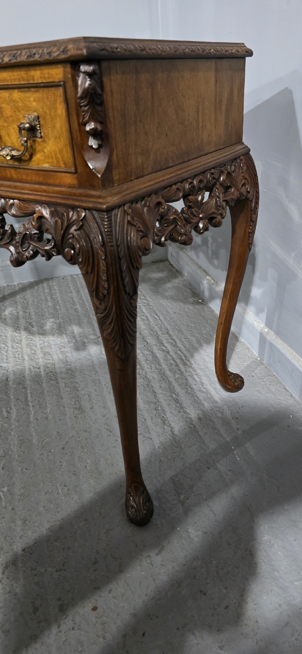 A burr walnut console table featuring two drawers with brass handles, a deeply carved apron with a central shell motif, and cabriole legs. View V