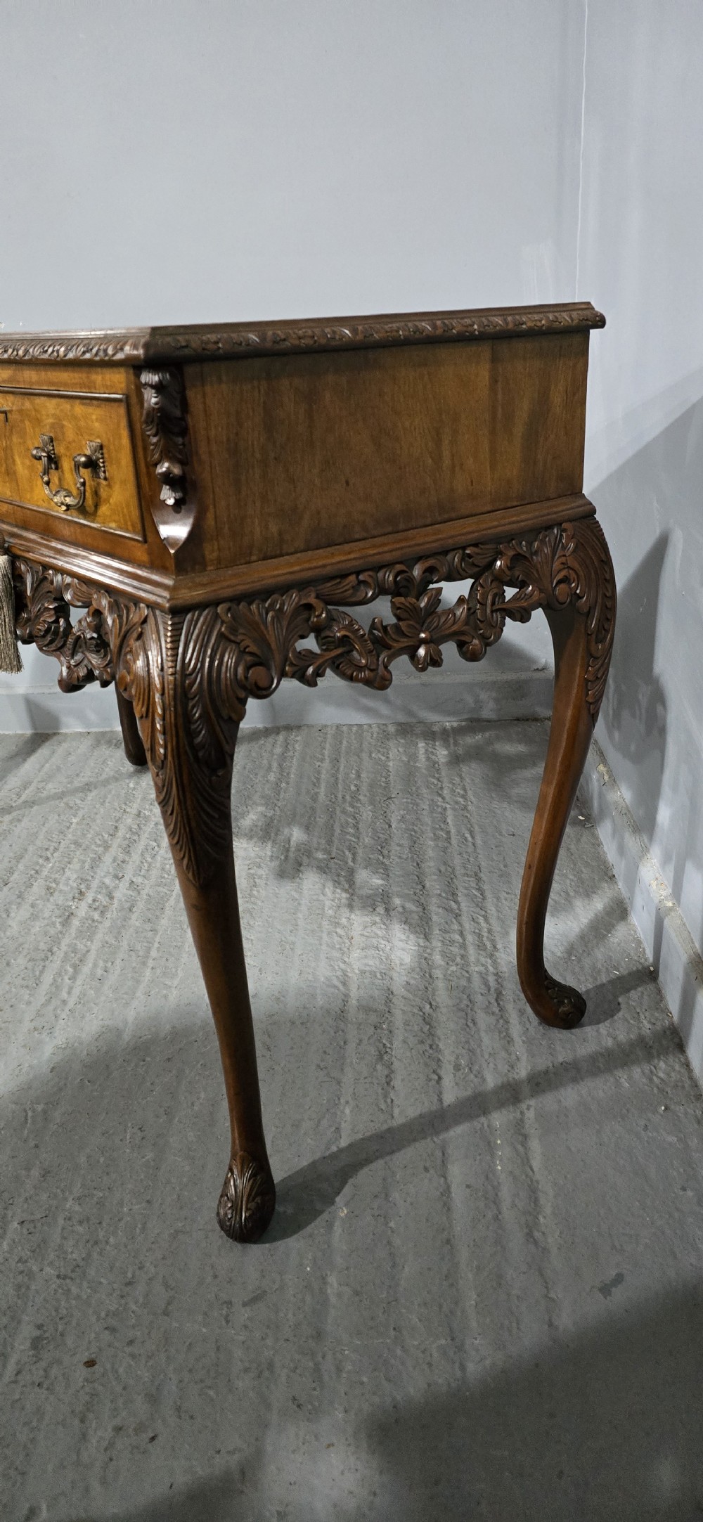A burr walnut console table featuring two drawers with brass handles, a deeply carved apron with a central shell motif, and cabriole legs. View VI