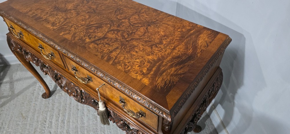 A burr walnut console table featuring two drawers with brass handles, a deeply carved apron with a central shell motif, and cabriole legs. View VII