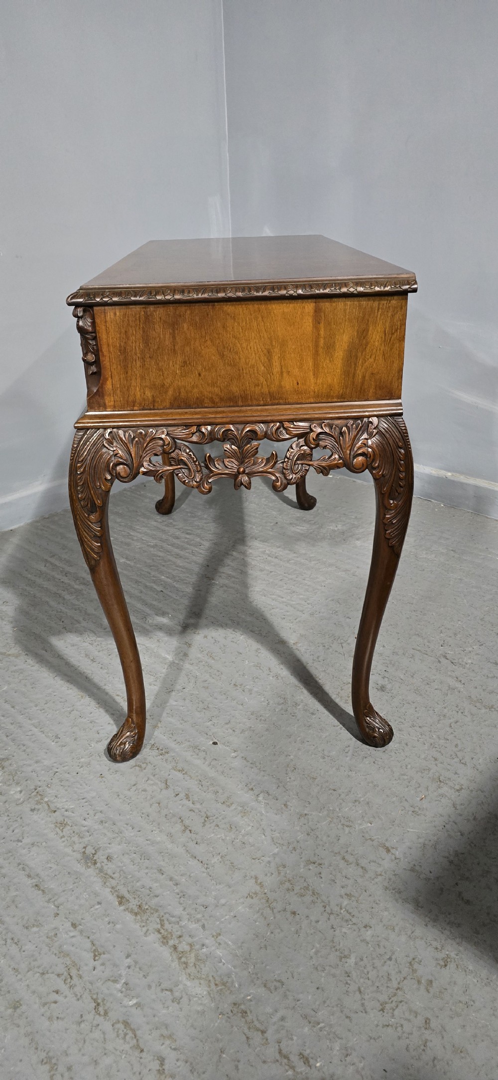 A burr walnut console table featuring two drawers with brass handles, a deeply carved apron with a central shell motif, and cabriole legs. View XIII