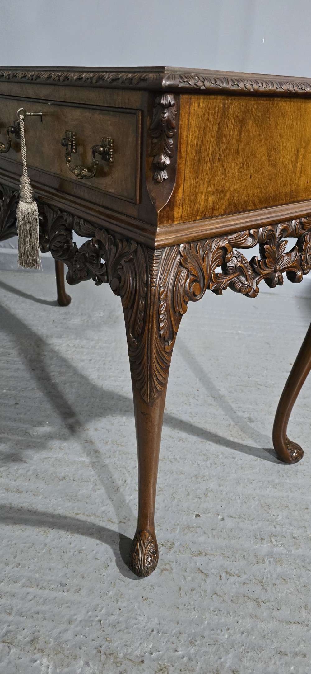 A burr walnut console table featuring two drawers with brass handles, a deeply carved apron with a central shell motif, and cabriole legs. View XV