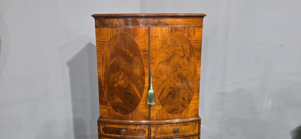 A Georgian mahogany bow-front linen press featuring oval flame mahogany inlay on the twin cupboard doors above four long graduated drawers. View V
