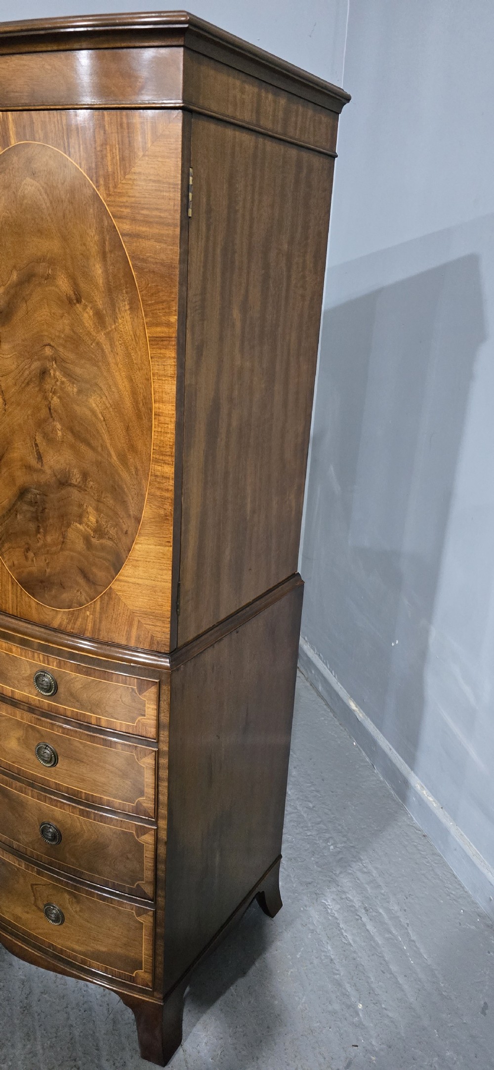 A Georgian mahogany bow-front linen press featuring oval flame mahogany inlay on the twin cupboard doors above four long graduated drawers. View VI