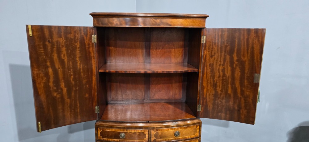 A Georgian mahogany bow-front linen press featuring oval flame mahogany inlay on the twin cupboard doors above four long graduated drawers. View X