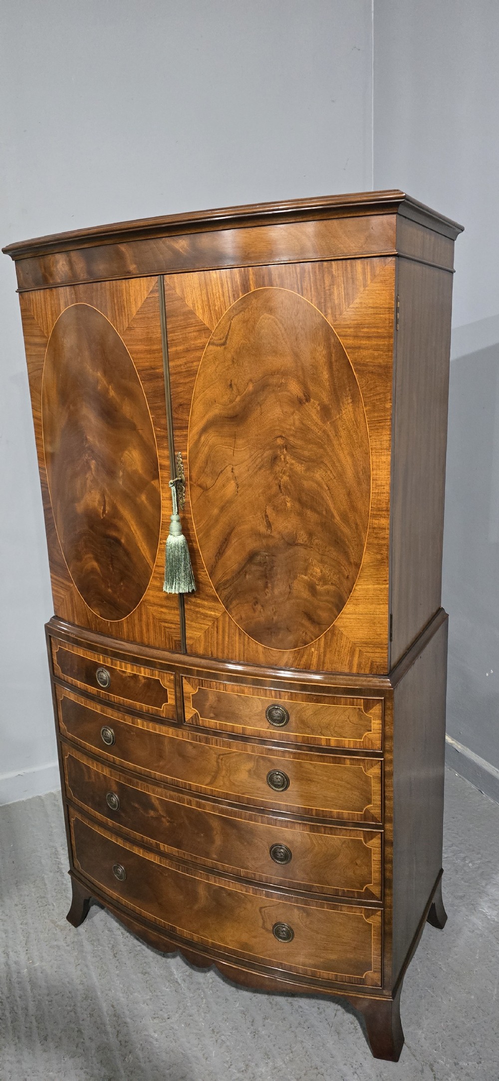 A Georgian mahogany bow-front linen press featuring oval flame mahogany inlay on the twin cupboard doors above four long graduated drawers. View XIII