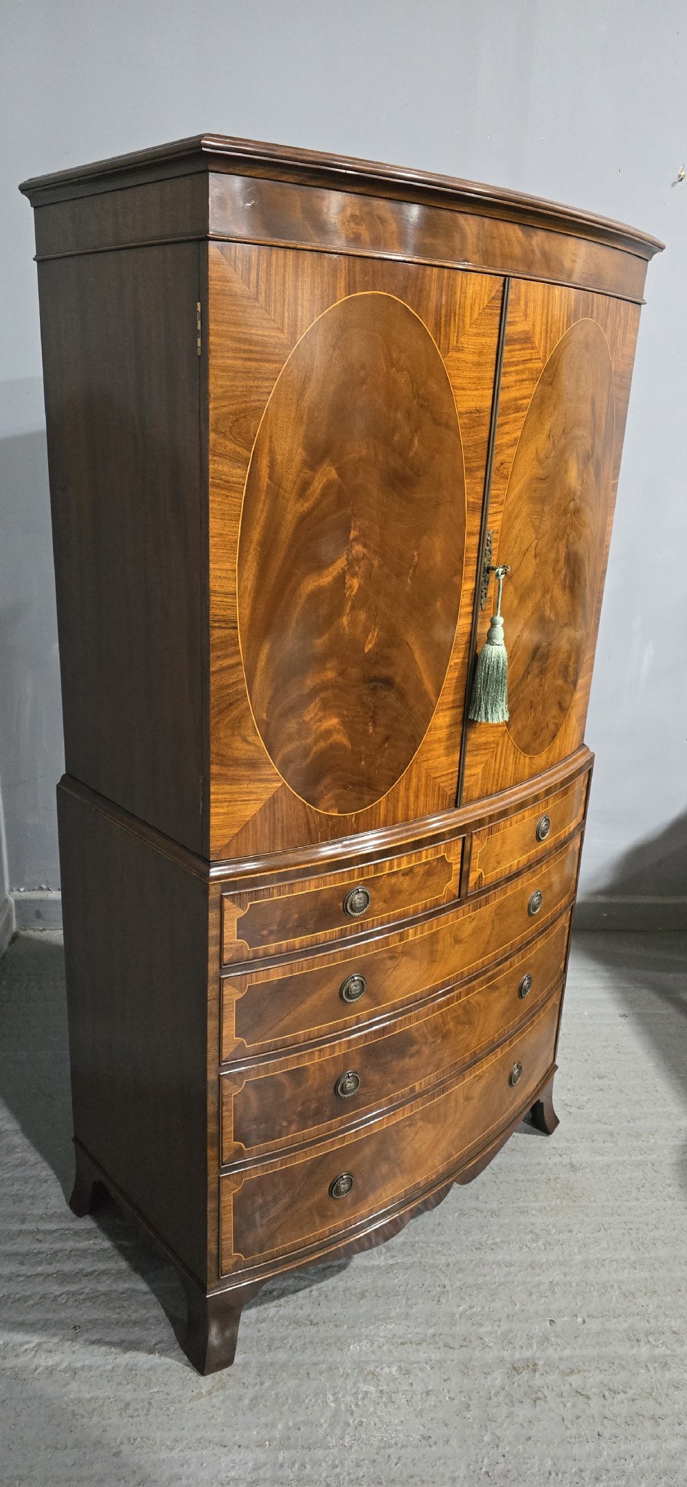 A Georgian mahogany bow-front linen press featuring oval flame mahogany inlay on the twin cupboard doors above four long graduated drawers. View XIV
