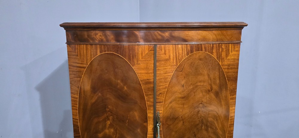 A Georgian mahogany bow-front linen press featuring oval flame mahogany inlay on the twin cupboard doors above four long graduated drawers. View XV