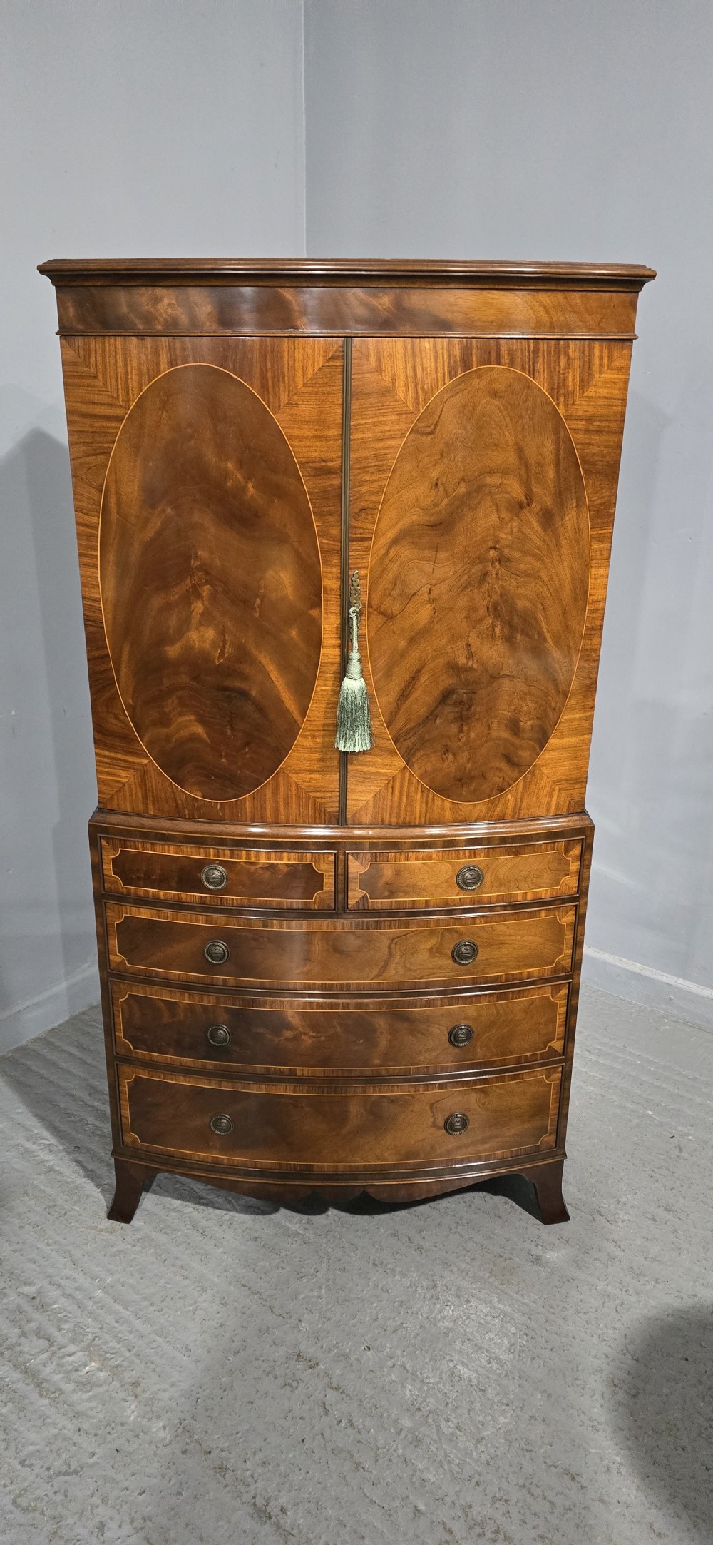 A Georgian mahogany bow-front linen press featuring oval flame mahogany inlay on the twin cupboard doors above four long graduated drawers. View XVI