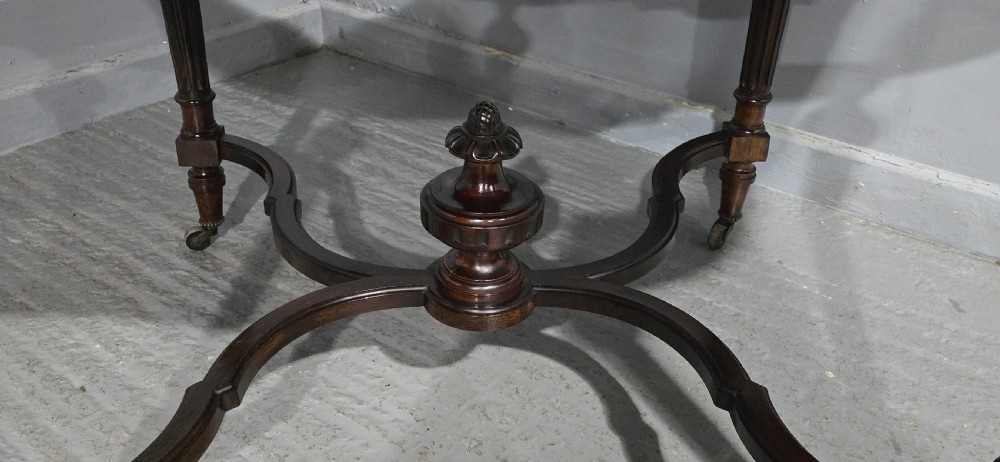 An antique dark brown wood library table featuring a leather inset top, carved frieze, turned legs, cross stretchers with a central finial, and brass castors. View VIII