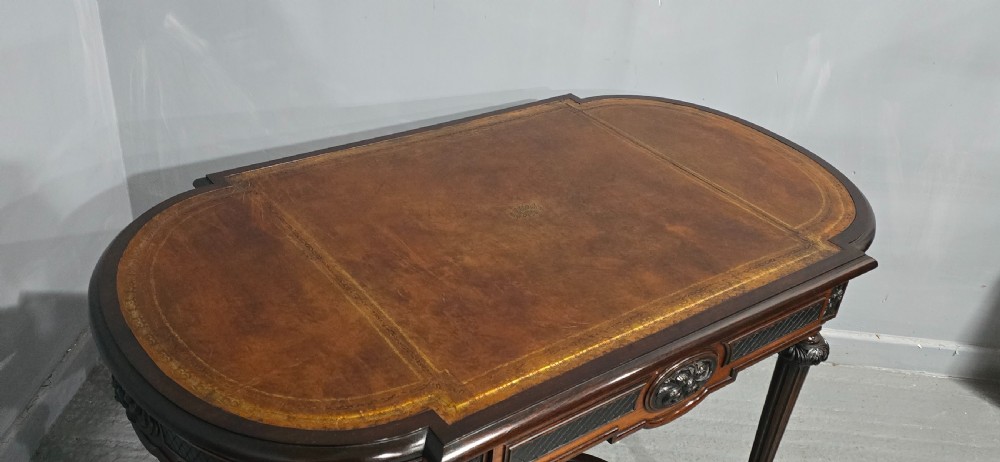 An antique dark brown wood library table featuring a leather inset top, carved frieze, turned legs, cross stretchers with a central finial, and brass castors. View X