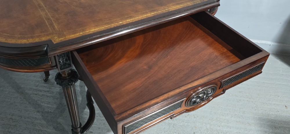 An antique dark brown wood library table featuring a leather inset top, carved frieze, turned legs, cross stretchers with a central finial, and brass castors. View XI