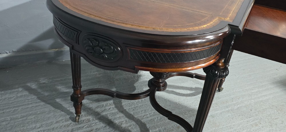 An antique dark brown wood library table featuring a leather inset top, carved frieze, turned legs, cross stretchers with a central finial, and brass castors. View XII