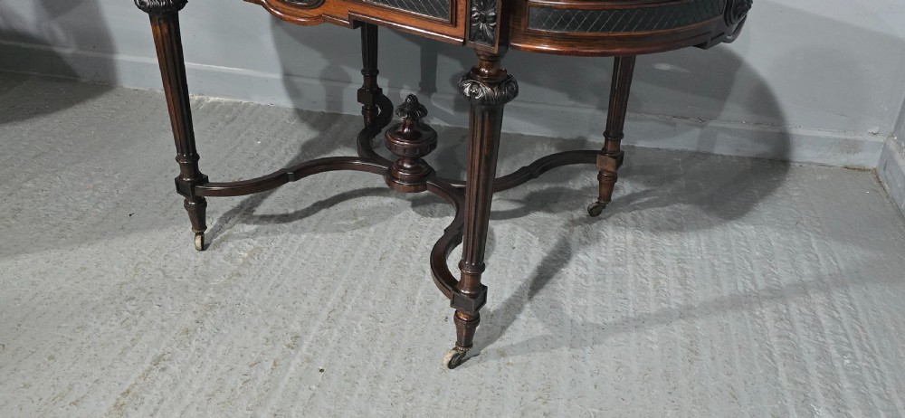 An antique dark brown wood library table featuring a leather inset top, carved frieze, turned legs, cross stretchers with a central finial, and brass castors. View XXIII