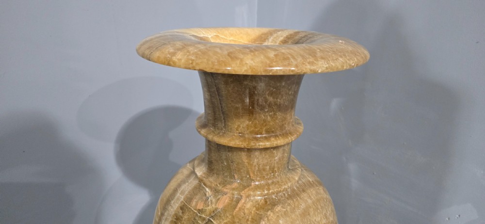 A large carved honey-brown alabaster vase featuring natural white veining, a flared rim, a knopped neck, and a stepped circular pedestal base. View VI
