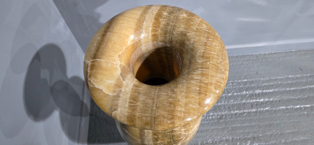 A large carved honey-brown alabaster vase featuring natural white veining, a flared rim, a knopped neck, and a stepped circular pedestal base. View VIII